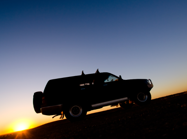 Silhouette of a pickup truck airborne against a sunset sky.